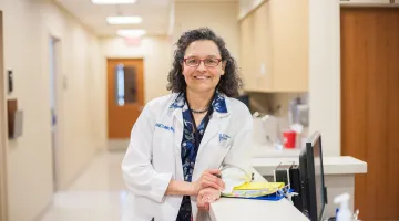 Doctor in lab coat leaning against a counter and smiling